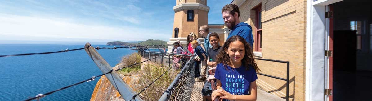 A small group of people stand near the Split Rock Lighthouse and look out over Lake Superior.