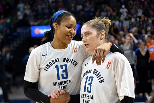 Two basketball players stand side by side, clasping two of their hands together.